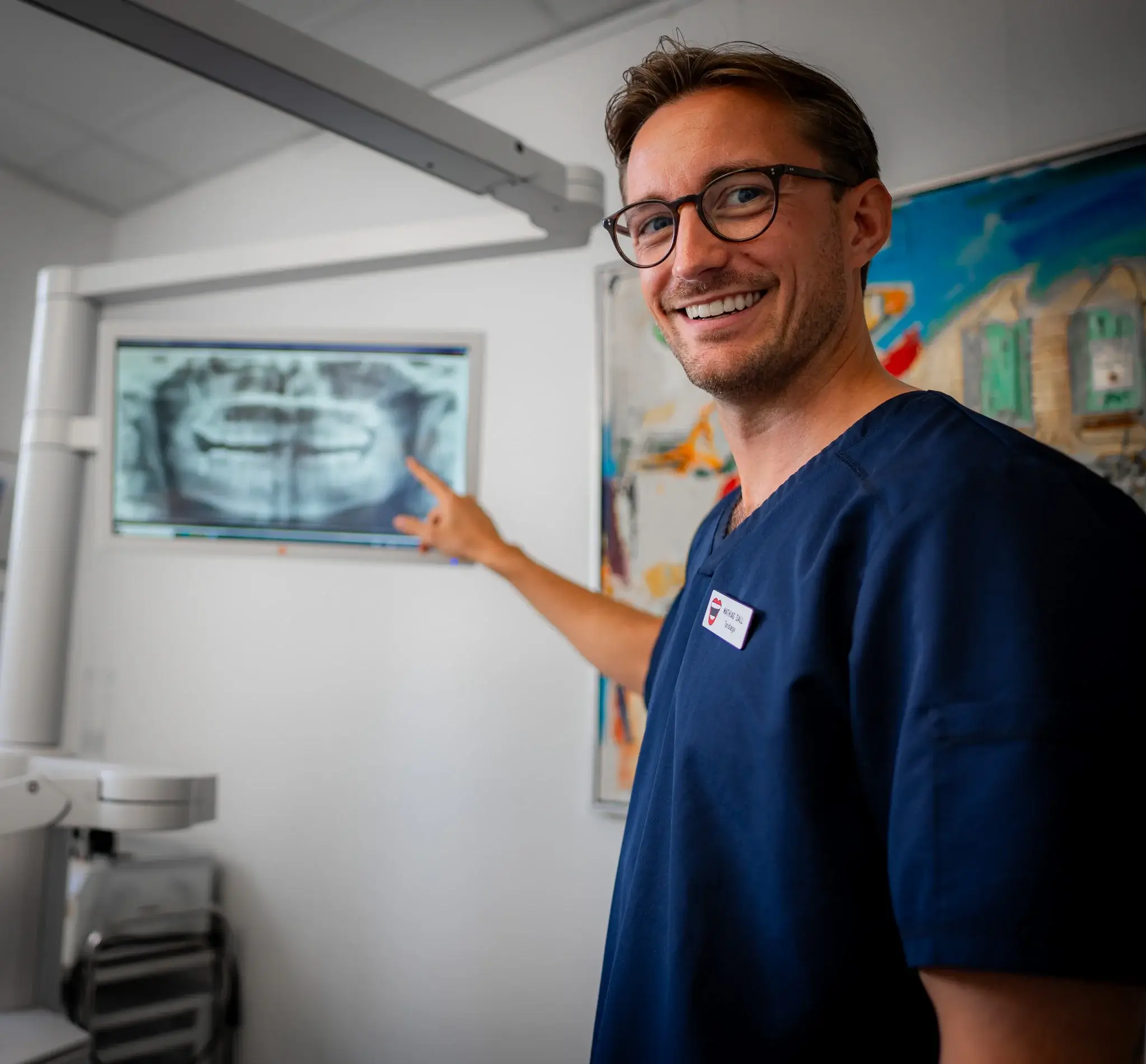 Tandlæge fra Østerbro Tandlægecenter smiler og peger på et røntgenbillede i den moderne klinik.