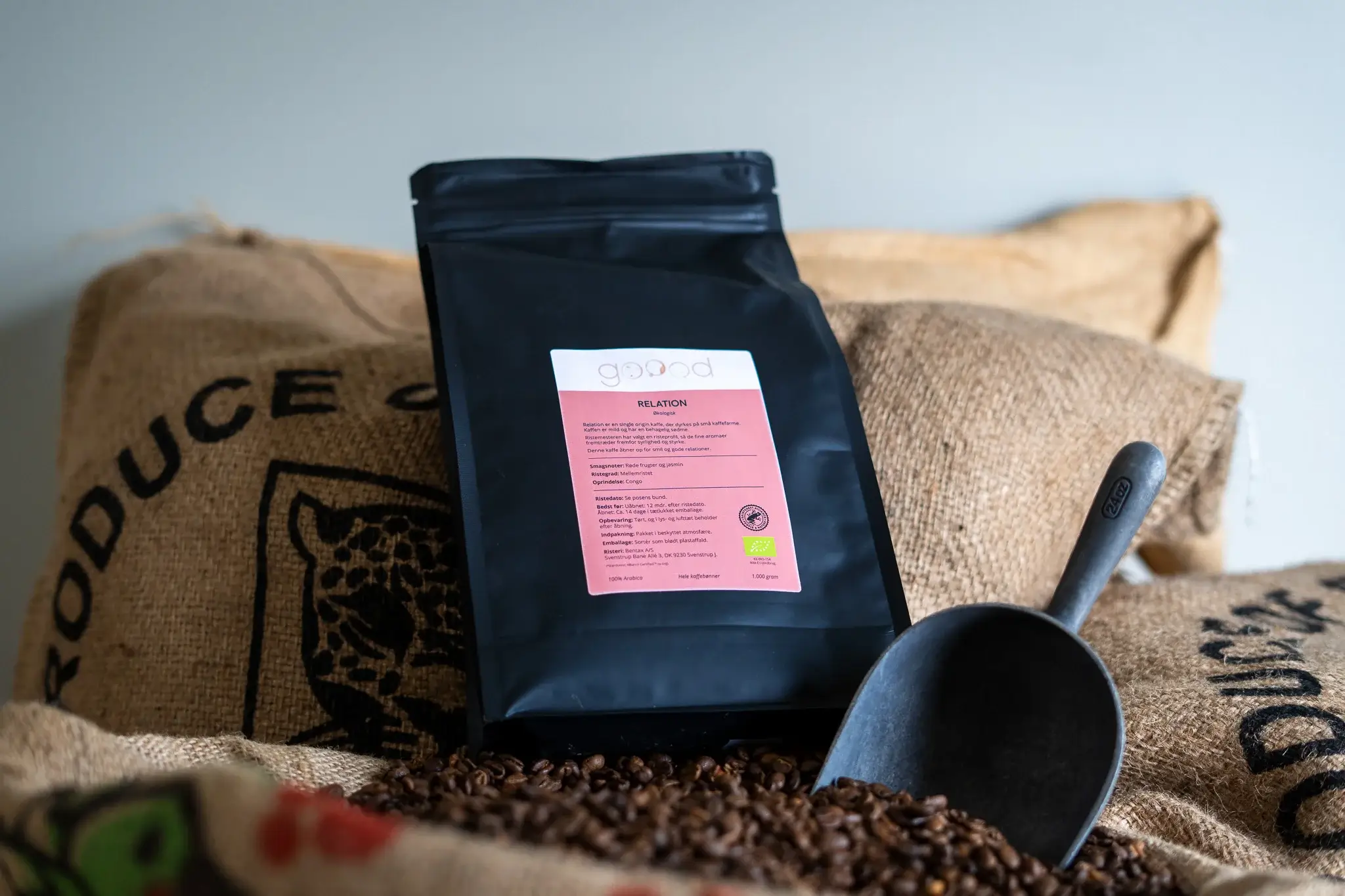affepose fra Goood Coffee Company placeret ovenpå kaffebønner og jutesække i et rustikt miljø.